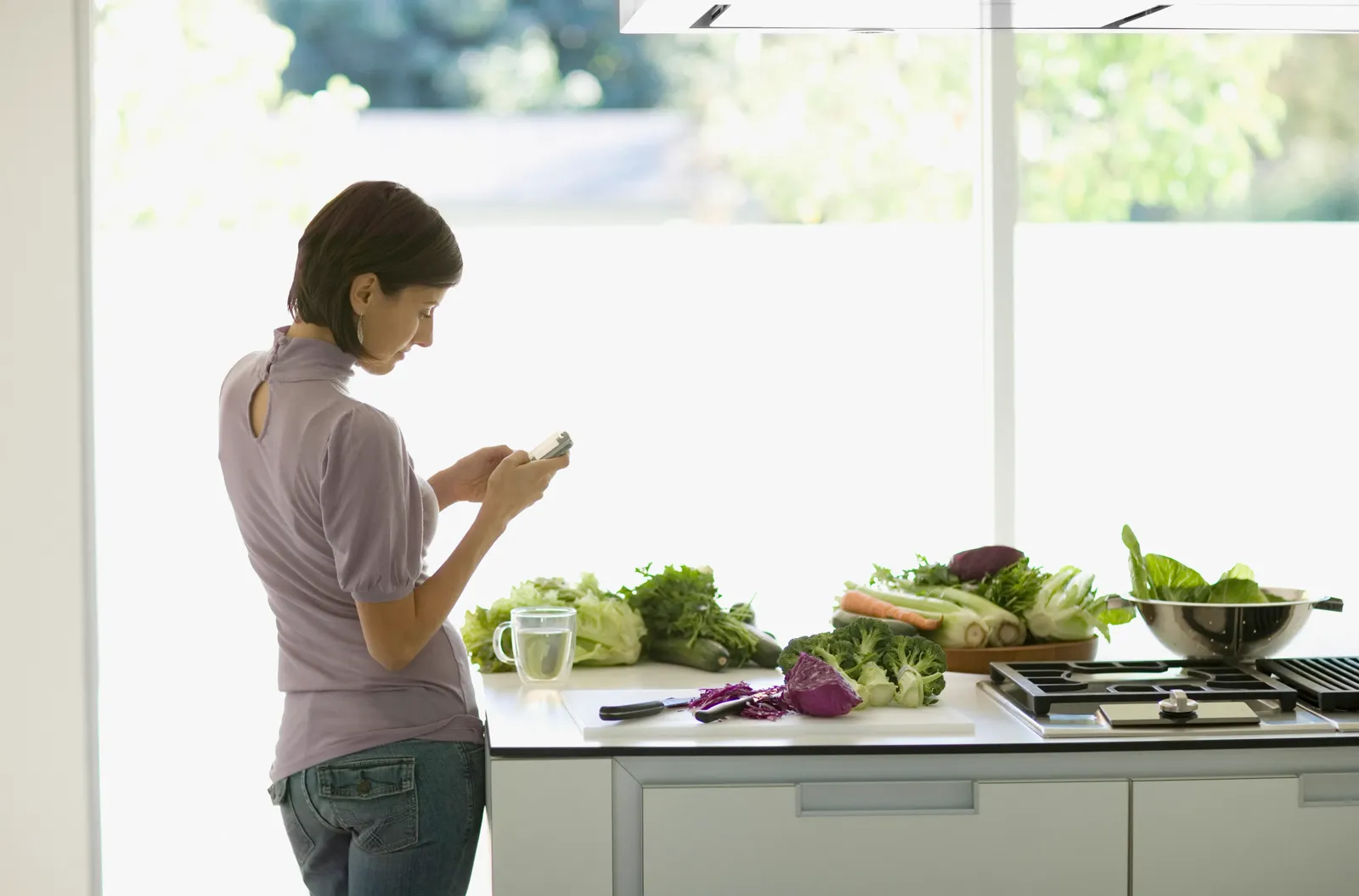 Woman in a bright kitchen pouring a glass of water beside fresh vegetables — the calcium and magnesium a remineralization stage puts back are the same minerals reverse osmosis strips out in the first place