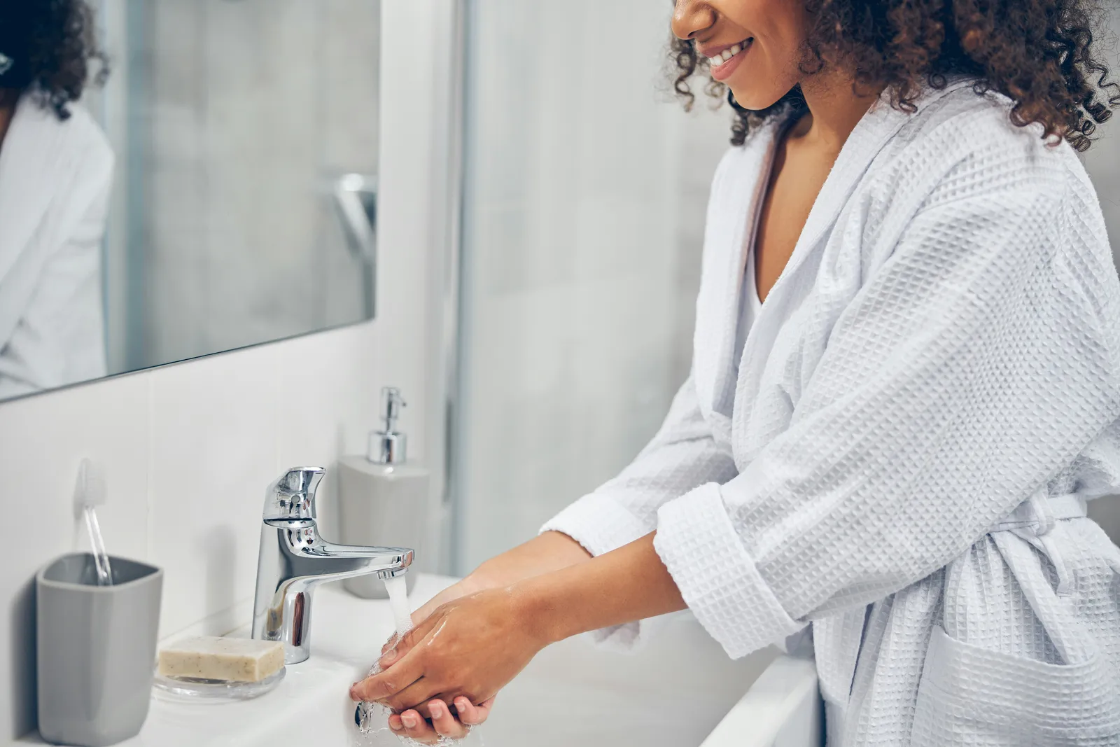Woman in a bathrobe washing her hands at a bathroom sink — on a well, every tap in the house draws from the same source