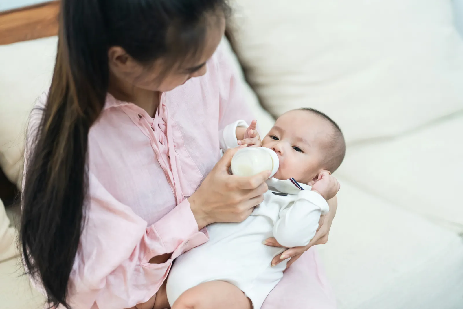 Mother bottle-feeding her baby in soft, bright window light