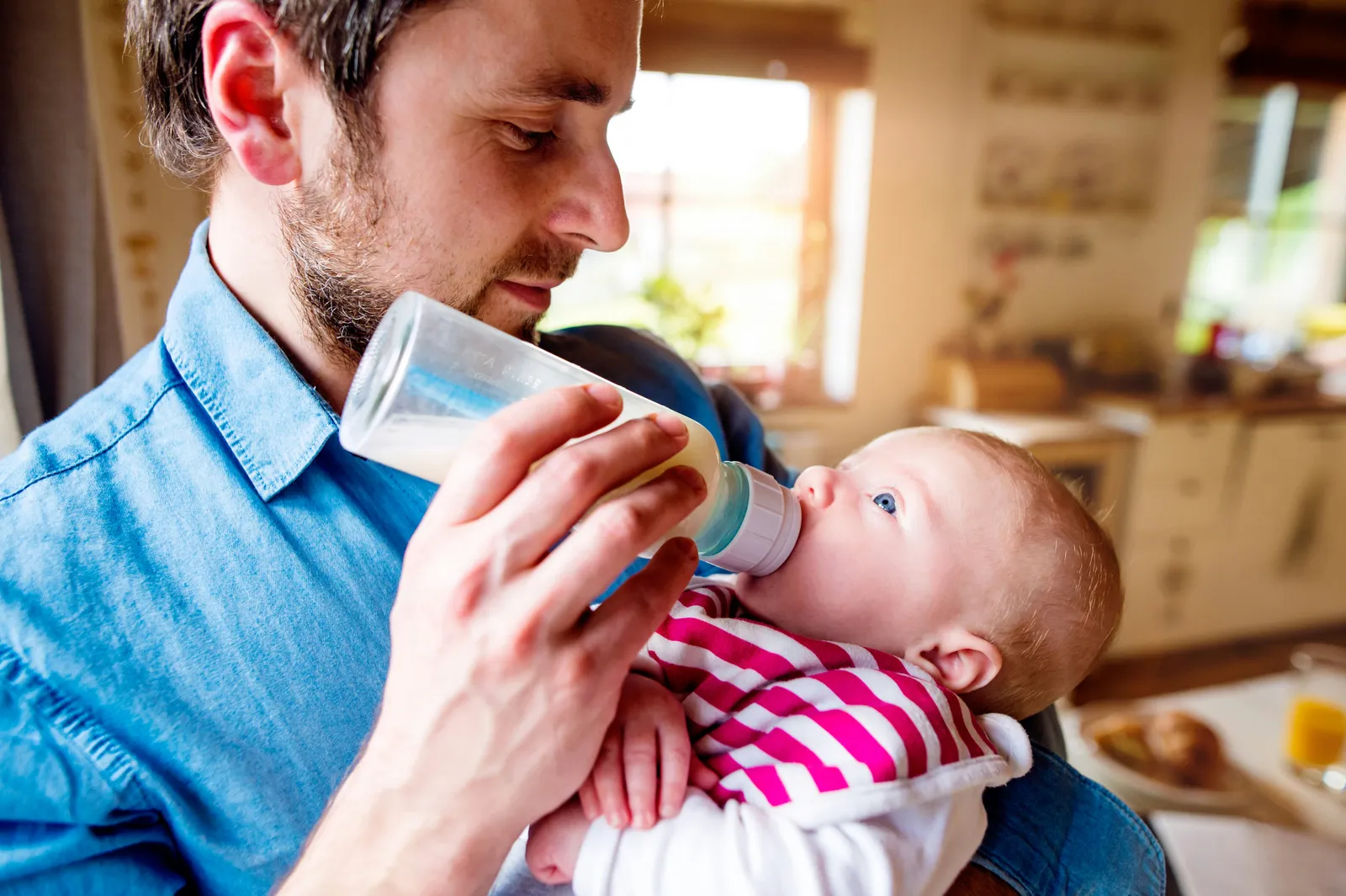 Father bottle-feeding his baby in a sunlit kitchen