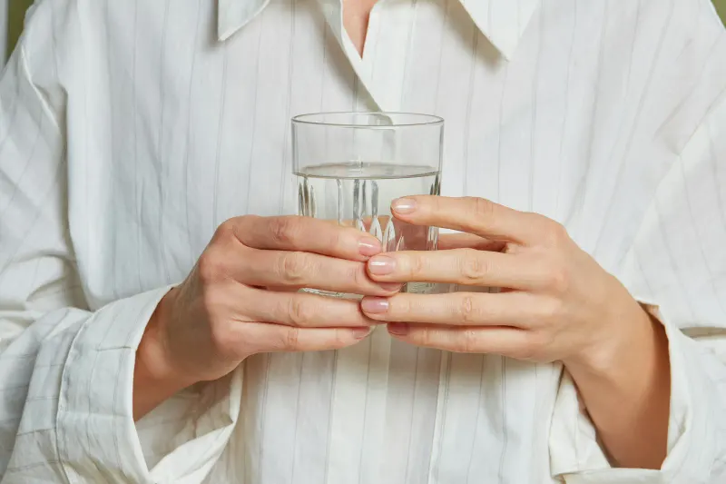 Hands holding a clear glass of water against a white linen shirt