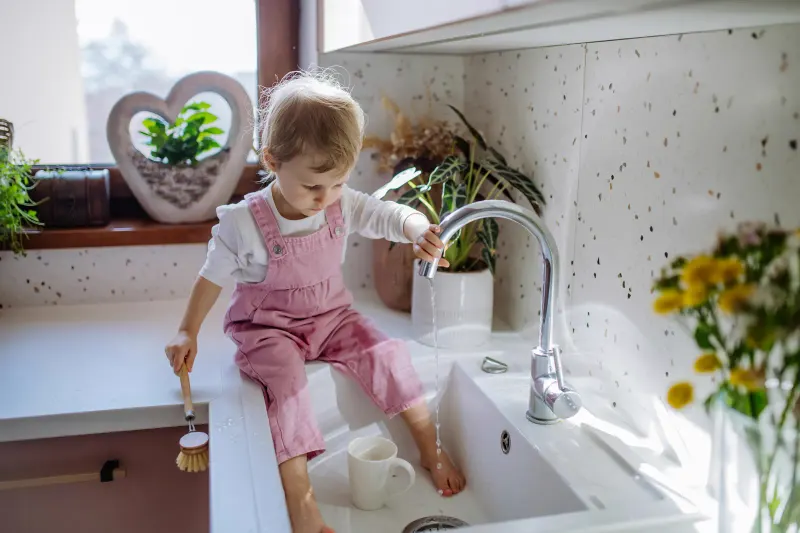 Child reaching up to turn on kitchen faucet — regular filter replacement is what keeps the water coming out of that tap clean