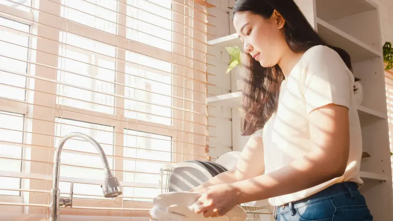 Woman at a kitchen sink in soft morning light from a shuttered window — deciding whether reverse osmosis is worth it starts at this tap
