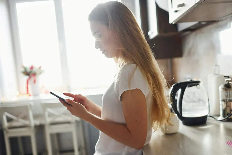 Woman reading on her phone in a bright kitchen — checking a filter's spec sheet before you buy