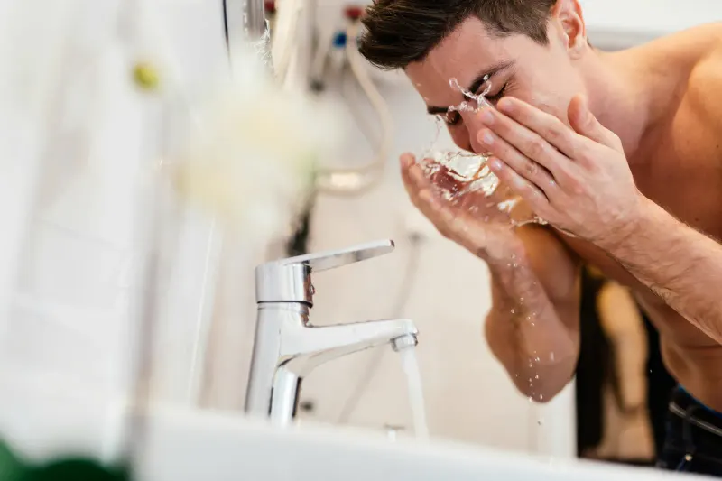 Man splashing water on face at a bathroom faucet — water quality affects every daily routine in a home on a private well