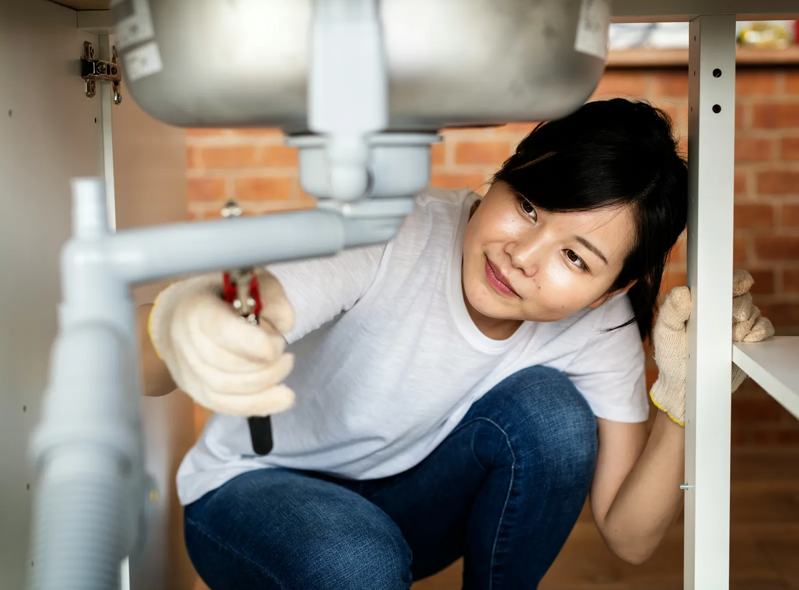 Woman fitting an under-sink connection herself with a wrench — a multi-stage carbon system is a do-it-yourself install