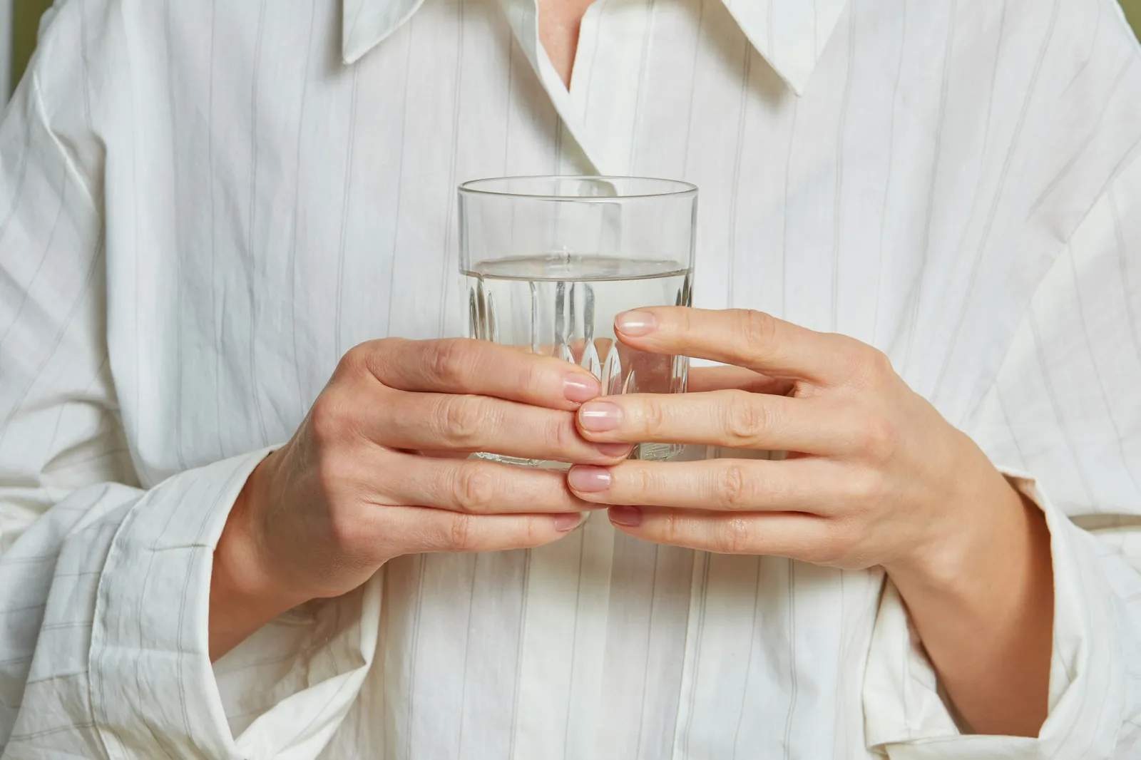 Hands holding a clear glass of water against a white linen shirt