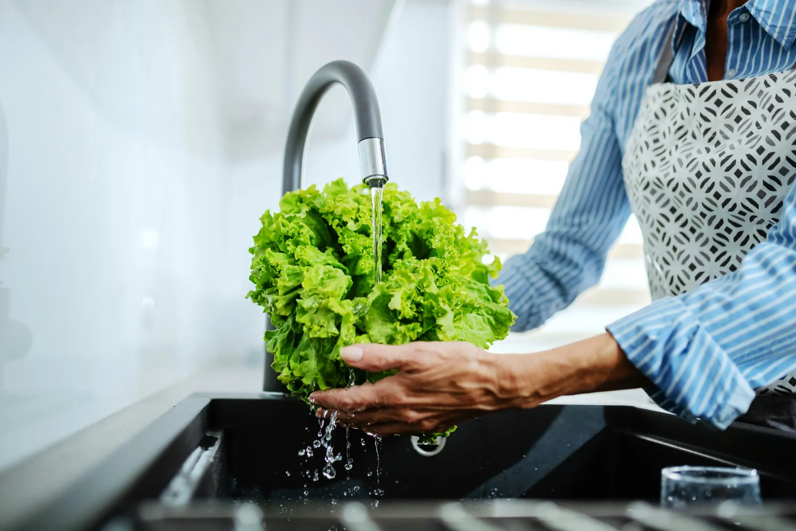 Woman rinsing a head of lettuce under the kitchen tap