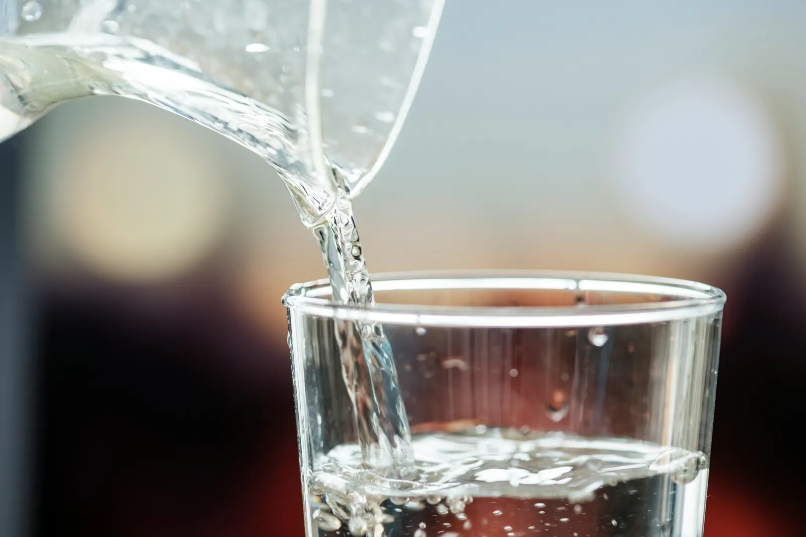 Water pouring from a jug into a clear glass, close up