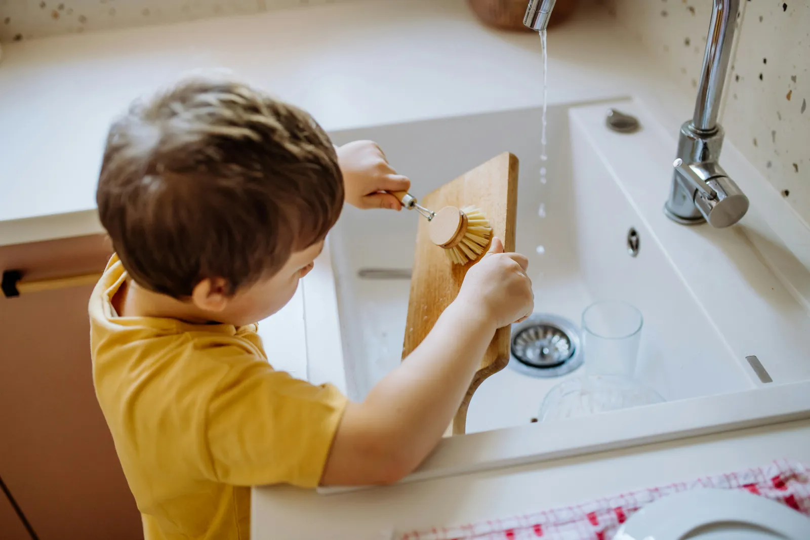 Young boy rinsing a cup at the kitchen sink — the same tap a family uses for drinking water and mixing a bottle