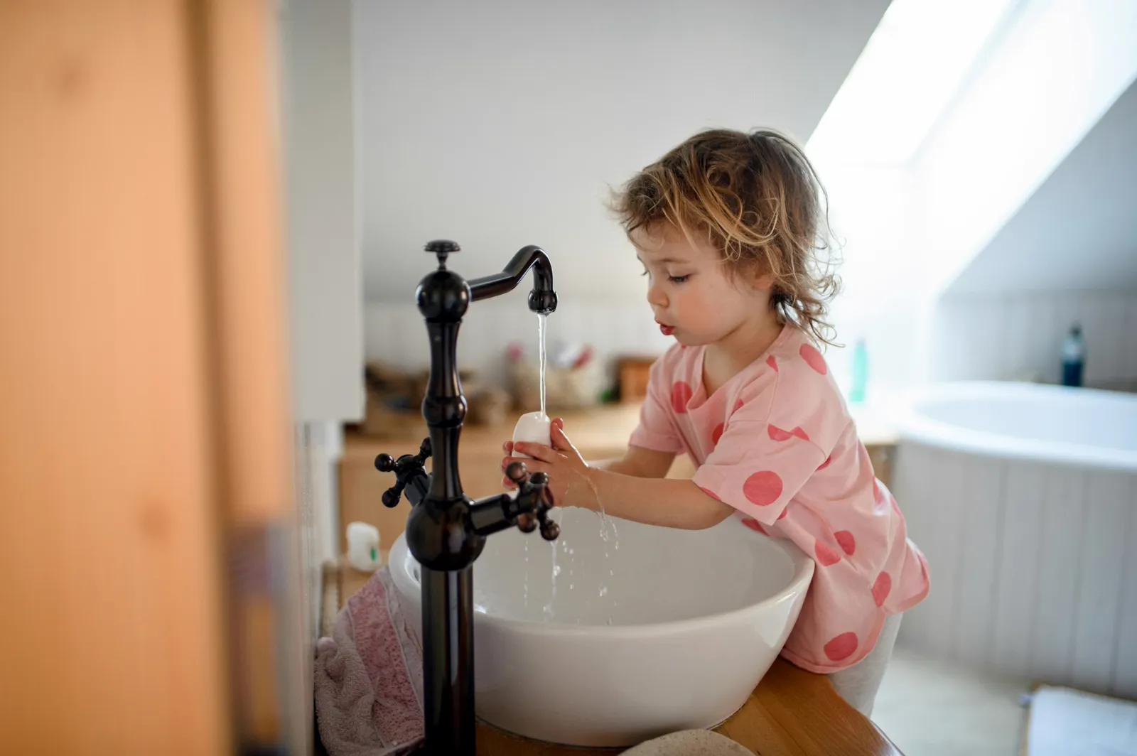 Young child learning to wash hands at kitchen faucet — a reminder that clean water matters most for children