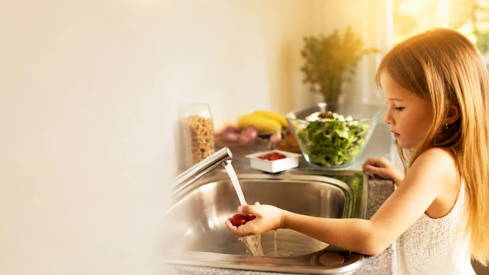 Young girl rinsing cherry tomatoes under the kitchen tap in bright morning light