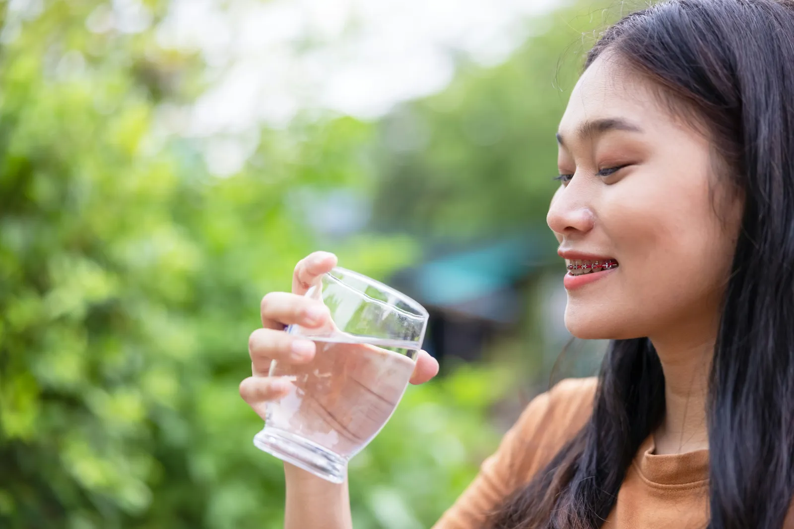 Woman drinking a glass of water outdoors in soft daylight