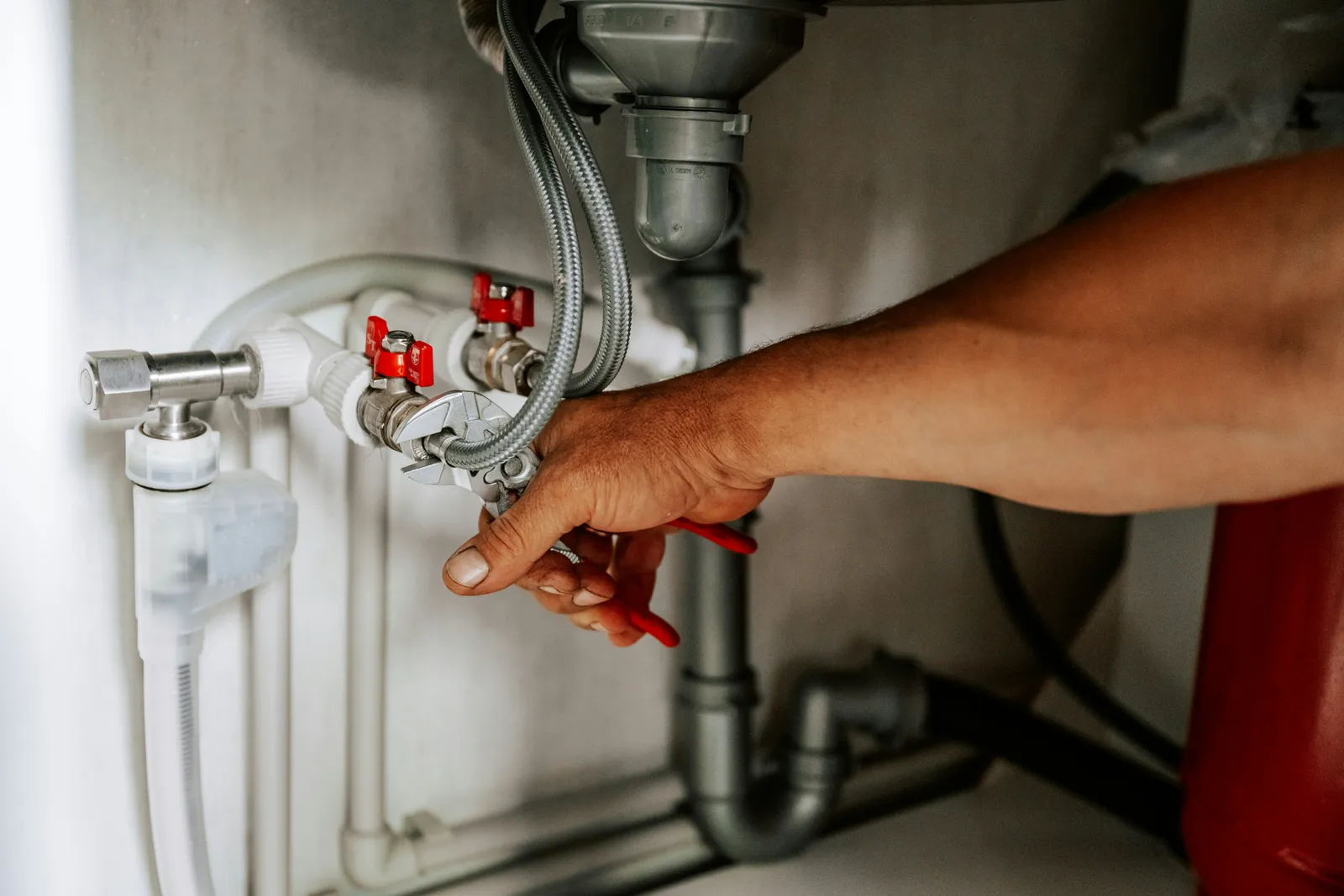 Hand on a shut-off valve under a kitchen sink, where a point-of-use water system connects