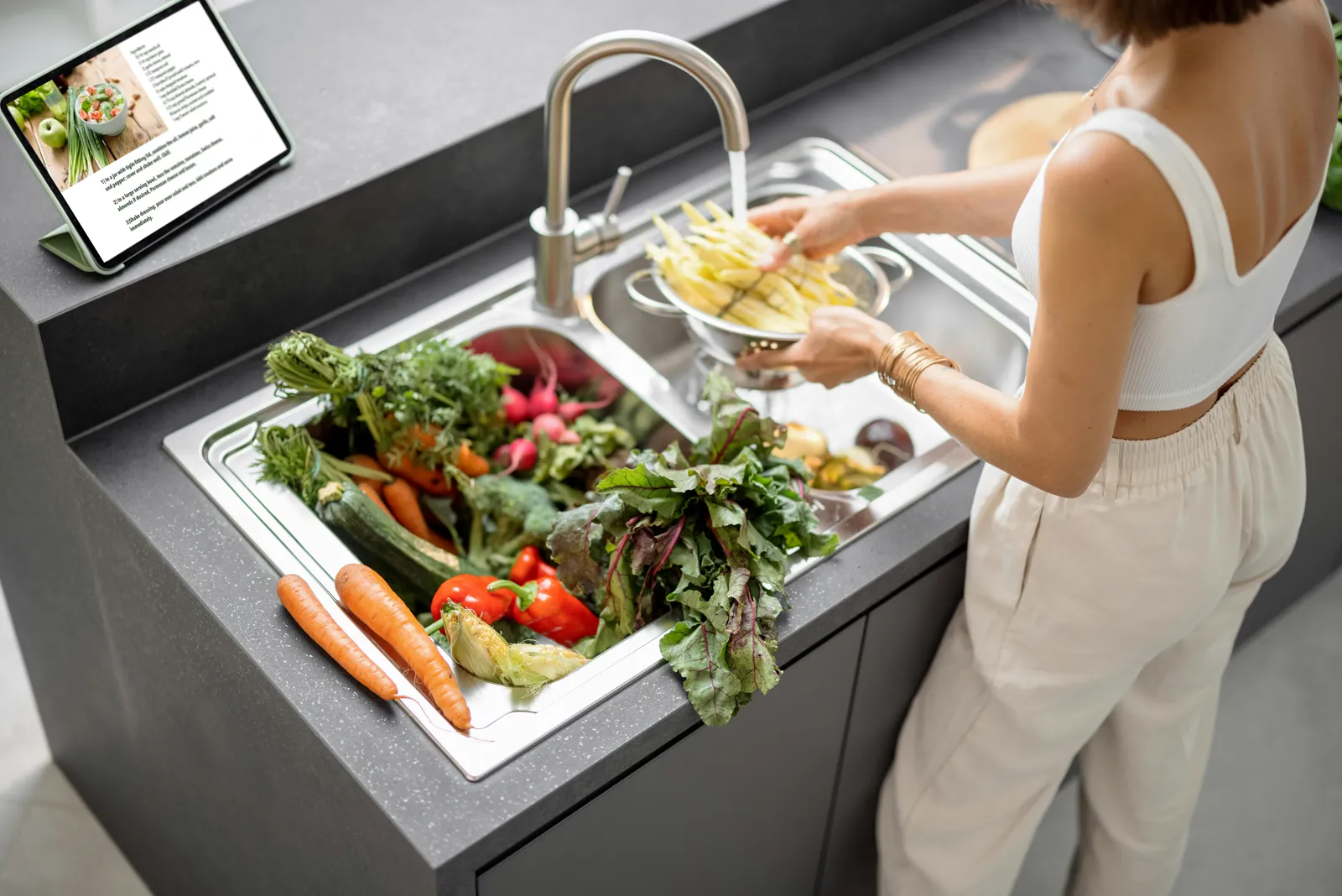 Person washing vegetables at a kitchen sink with filtered water running — a practical reminder that water quality affects cooking, not just drinking