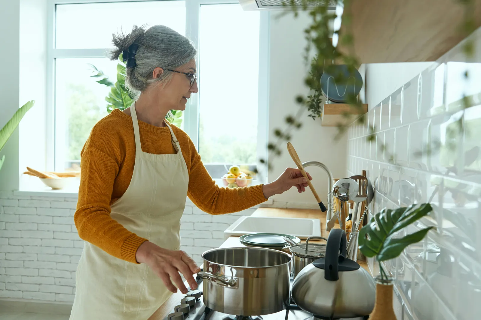 Woman in an apron cooking at the stove in a bright kitchen — the water food is cooked in carries its minerals, or the lack of them, into the meal