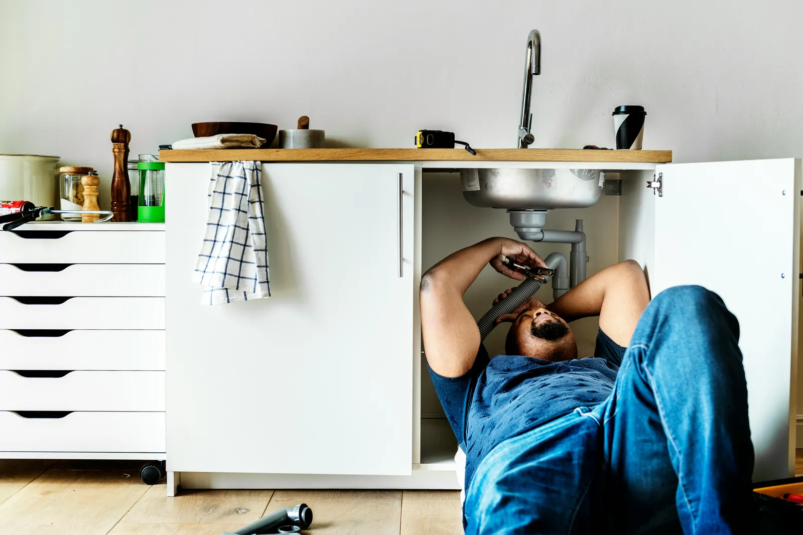 Plumber lying under an open kitchen sink cabinet fitting pipework — installation is part of what an RO system really costs