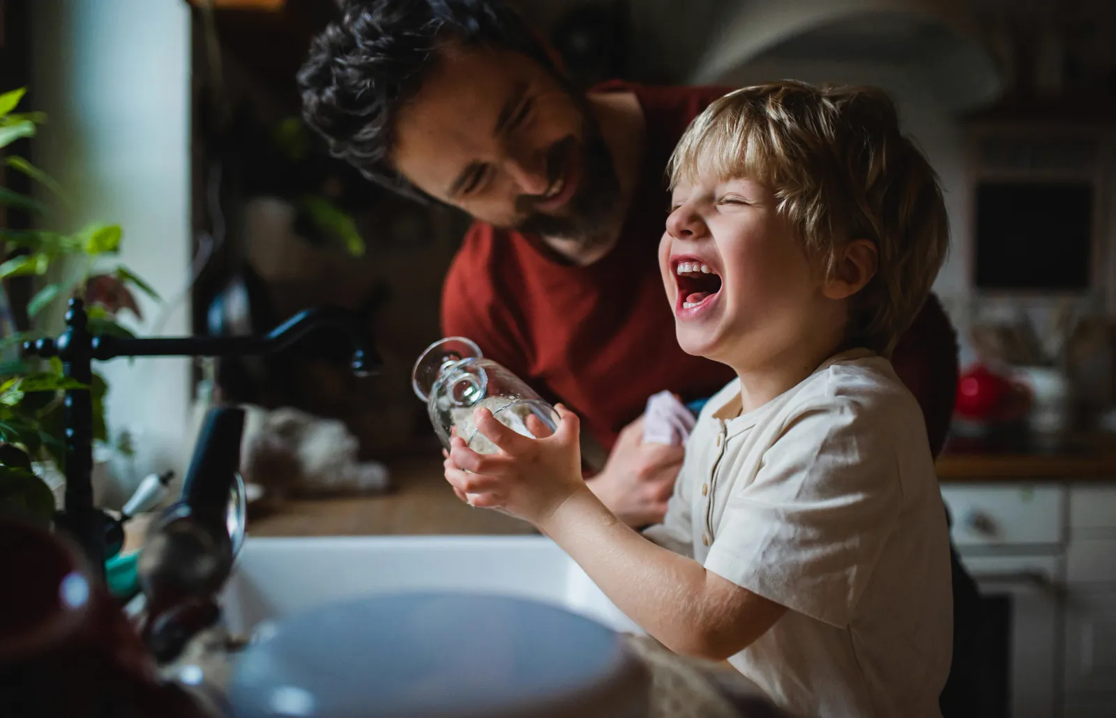 A parent and child at a kitchen sink filling a glass from the tap — deciding whether reverse osmosis is worth it starts with knowing what is actually in your water